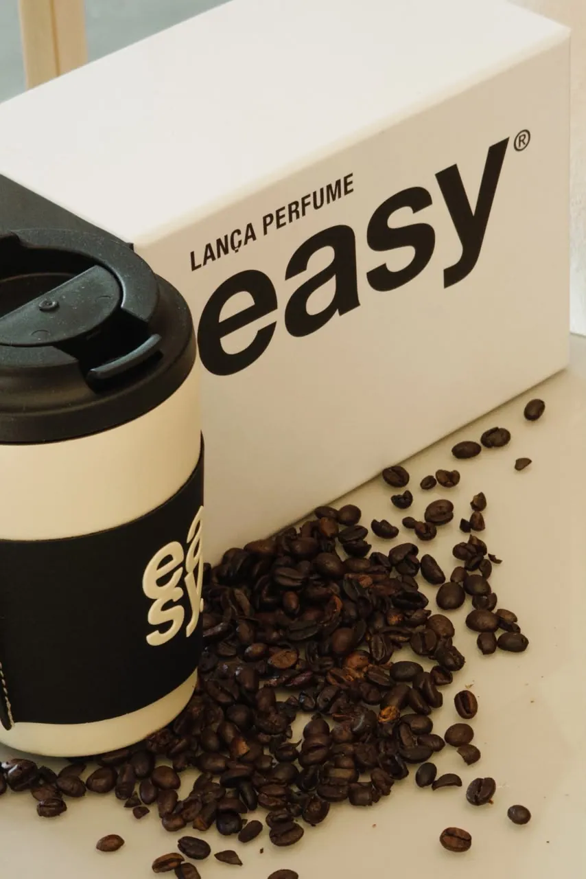 Caixa Lança Perfume easy e copo térmico sobre grãos de café em detalhe da vitrine