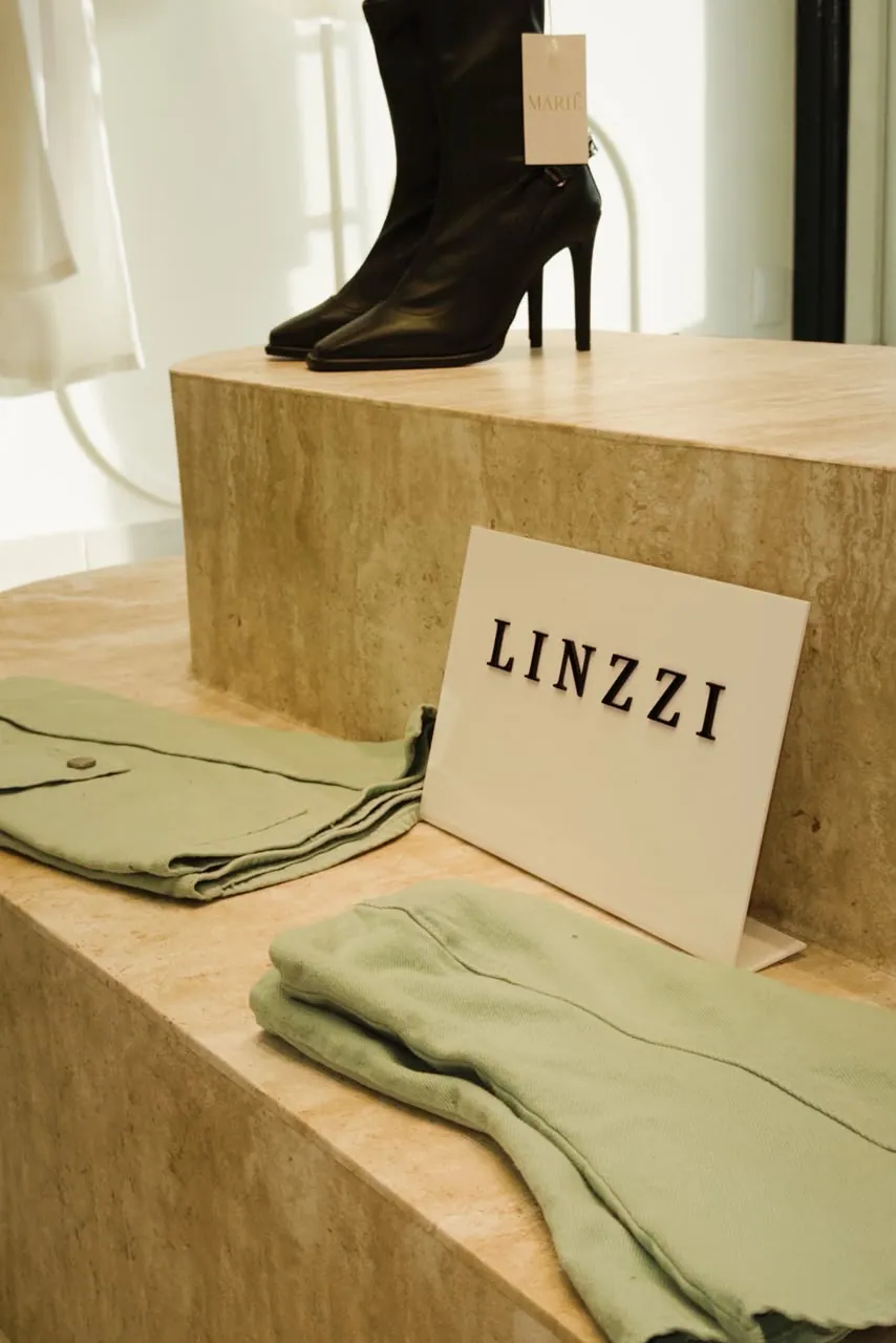 Bota preta de bico fino sobre expositor de travertino, ao lado da placa Linzzi
