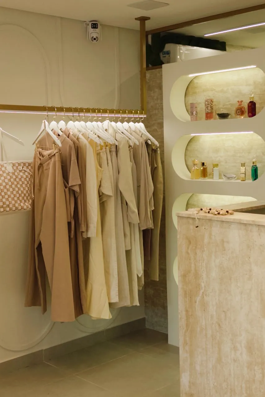 Vista do salão da Mariê com arara de tons neutros, nichos de perfumes e balcão de travertino