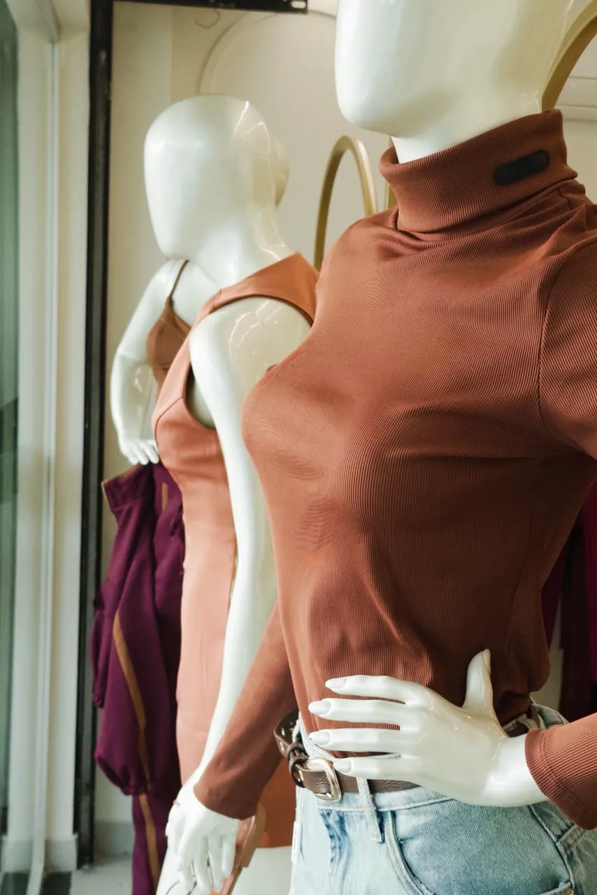 Manequim com blusa gola alta terracota, cinto e jeans claro na vitrine da Mariê