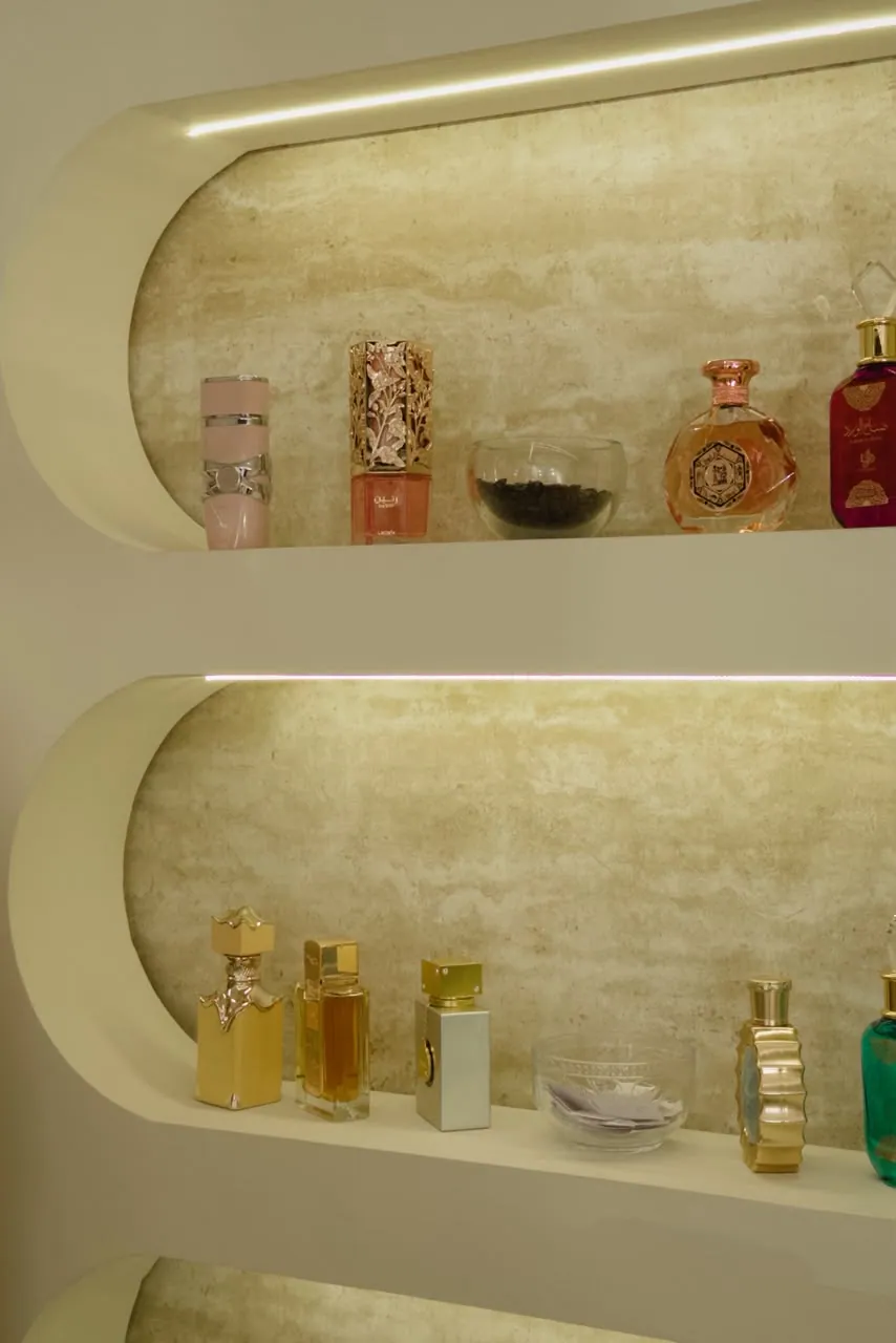Duas prateleiras curvas com perfumes árabes em frascos dourados e coloridos na Mariê